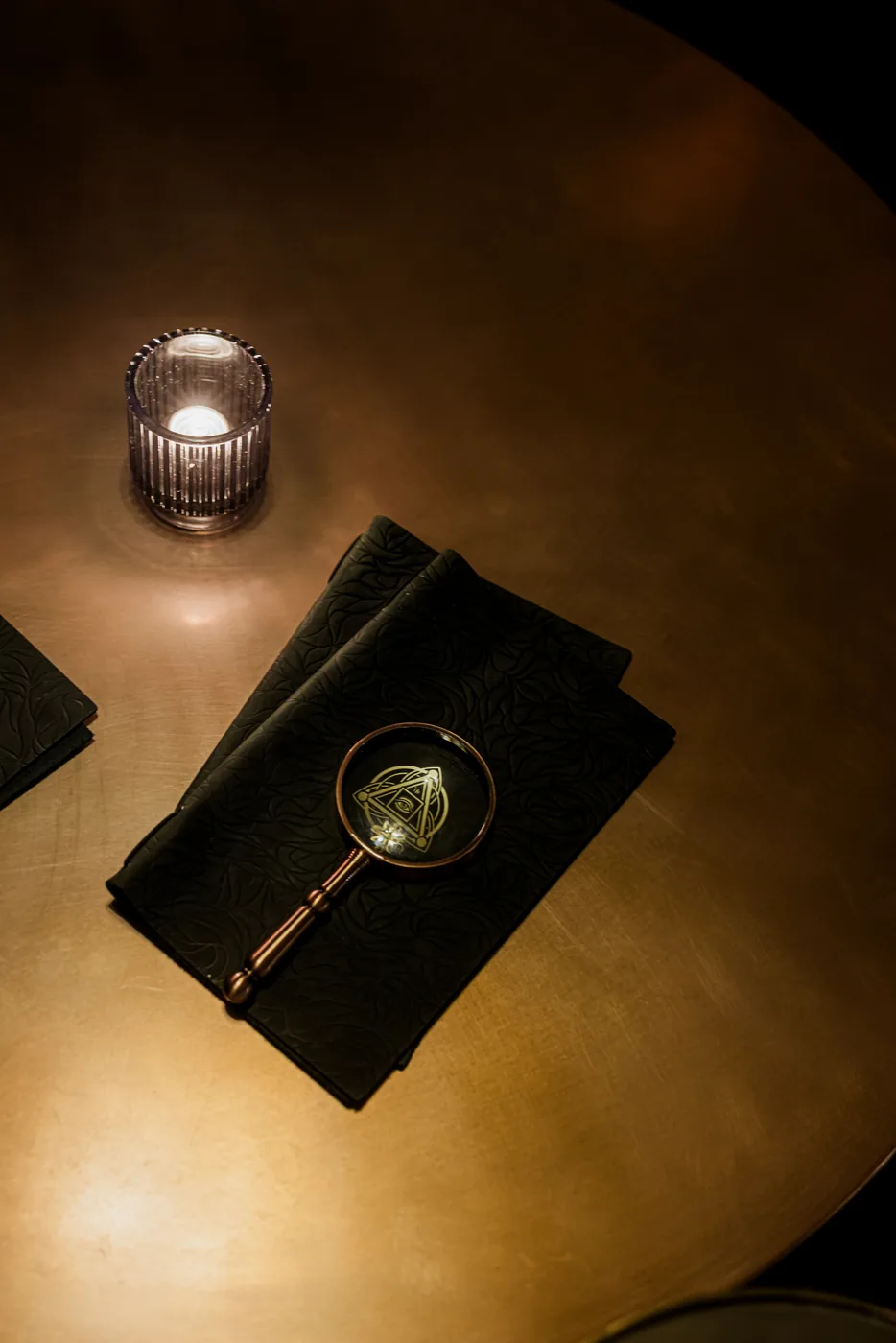 A lit candle and magnifying glass resting on a dark table at Anigma